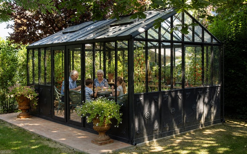 Grandparents and grandchildren eating summer lunch inside a black Janssens Helios Retro greenhouse