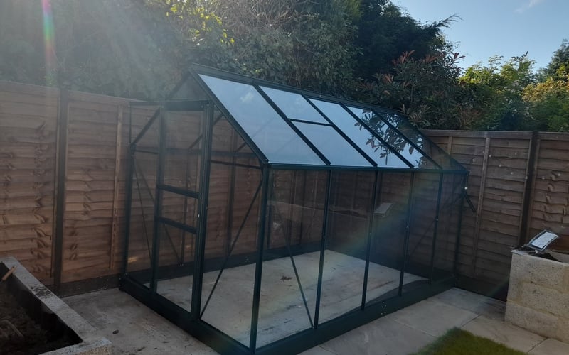Black aluminium greenhouse on a level lawn in a UK back garden
