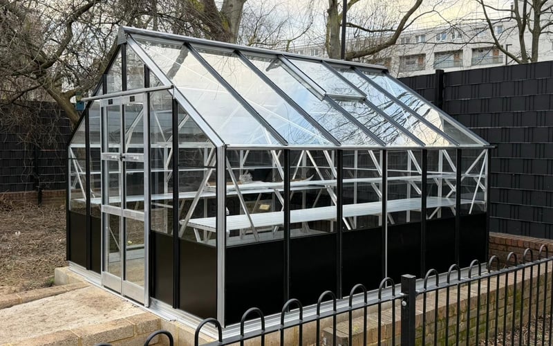 Black Janssens Victorian greenhouse with a roof finial and railings on a lawn