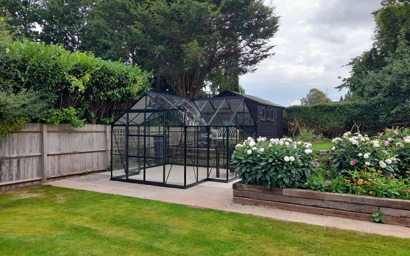 Black greenhouse used as a centrepiece on a wide lawn edged with roses