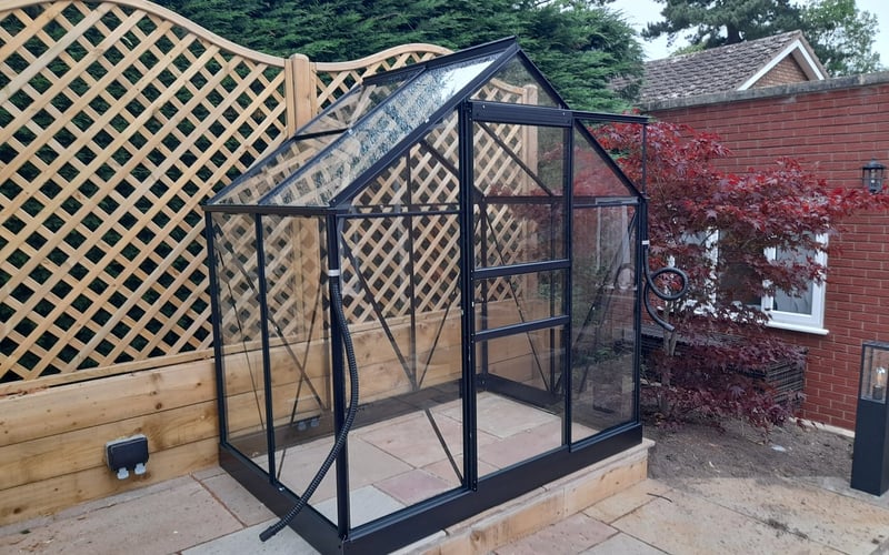 Black greenhouse set against a decorative trellis screen on block paving