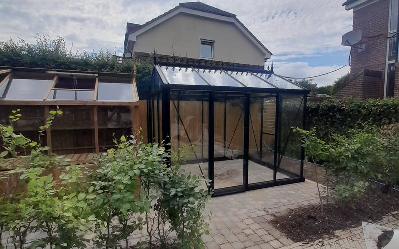 Black greenhouse paired with a wooden cold frame on a herringbone brick patio